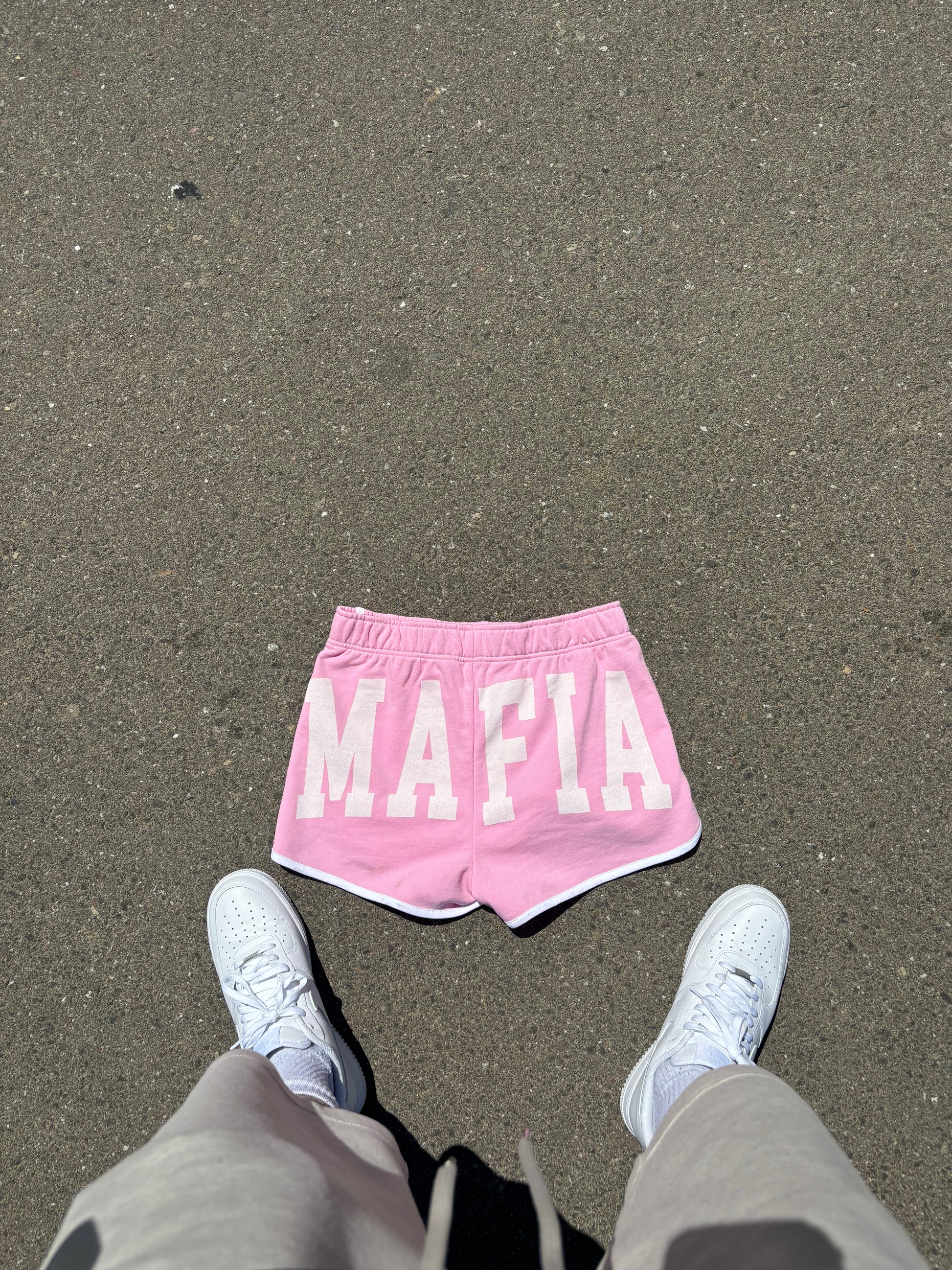 Back view of pink women’s streetwear shorts with bold white MAFIA lettering, photographed outdoors.