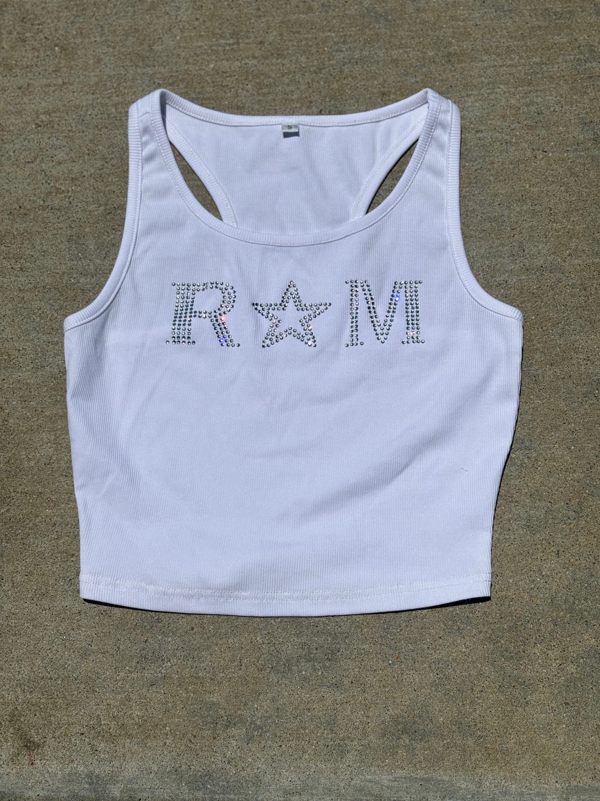 Close-up of a white ribbed crop top with rhinestone "RM" lettering and star worn with jeans – urban glam style by Renegade Mafia
