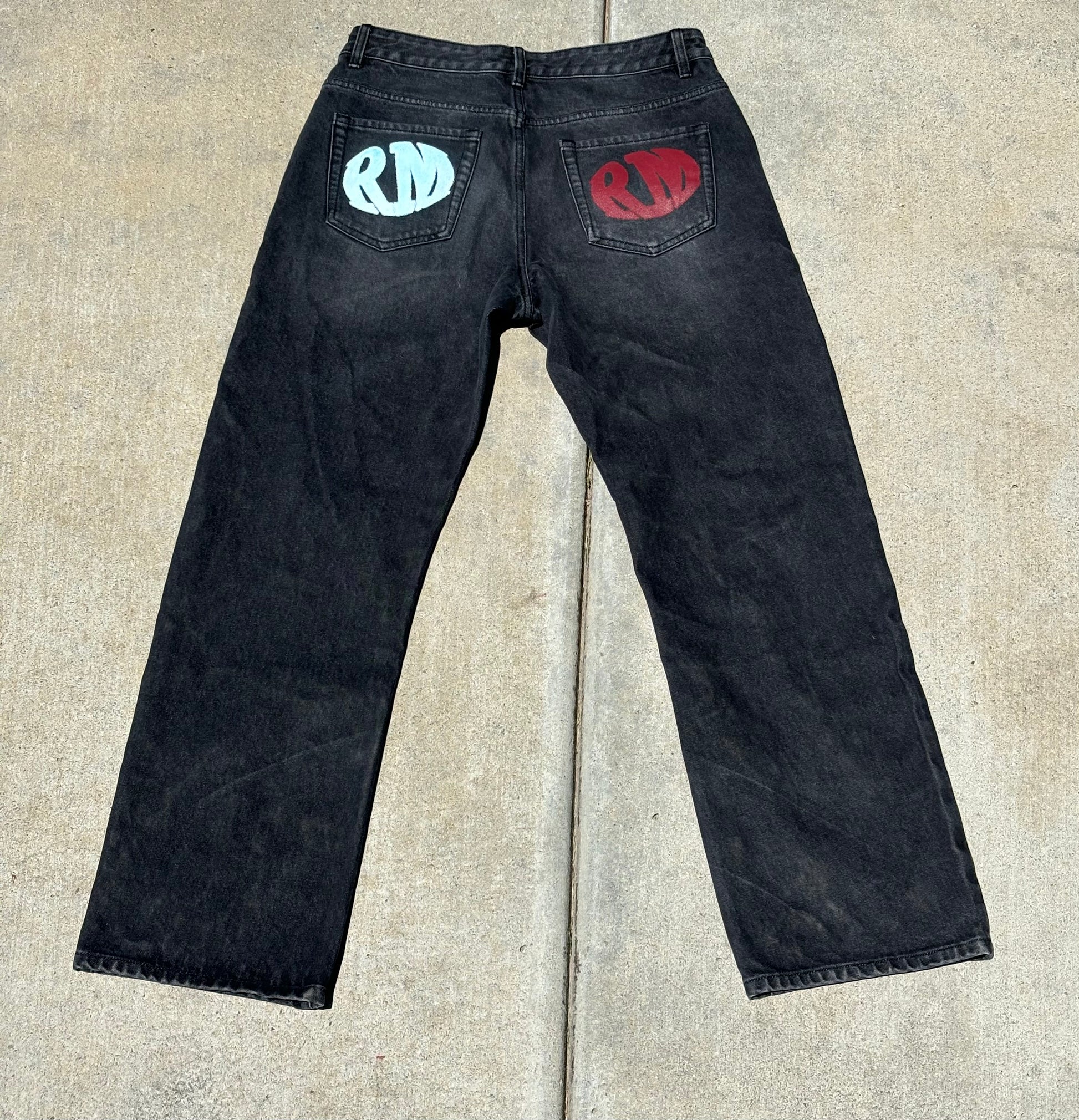 Back view of Renegade Mafia jeans featuring red and blue RM logos on both pockets”